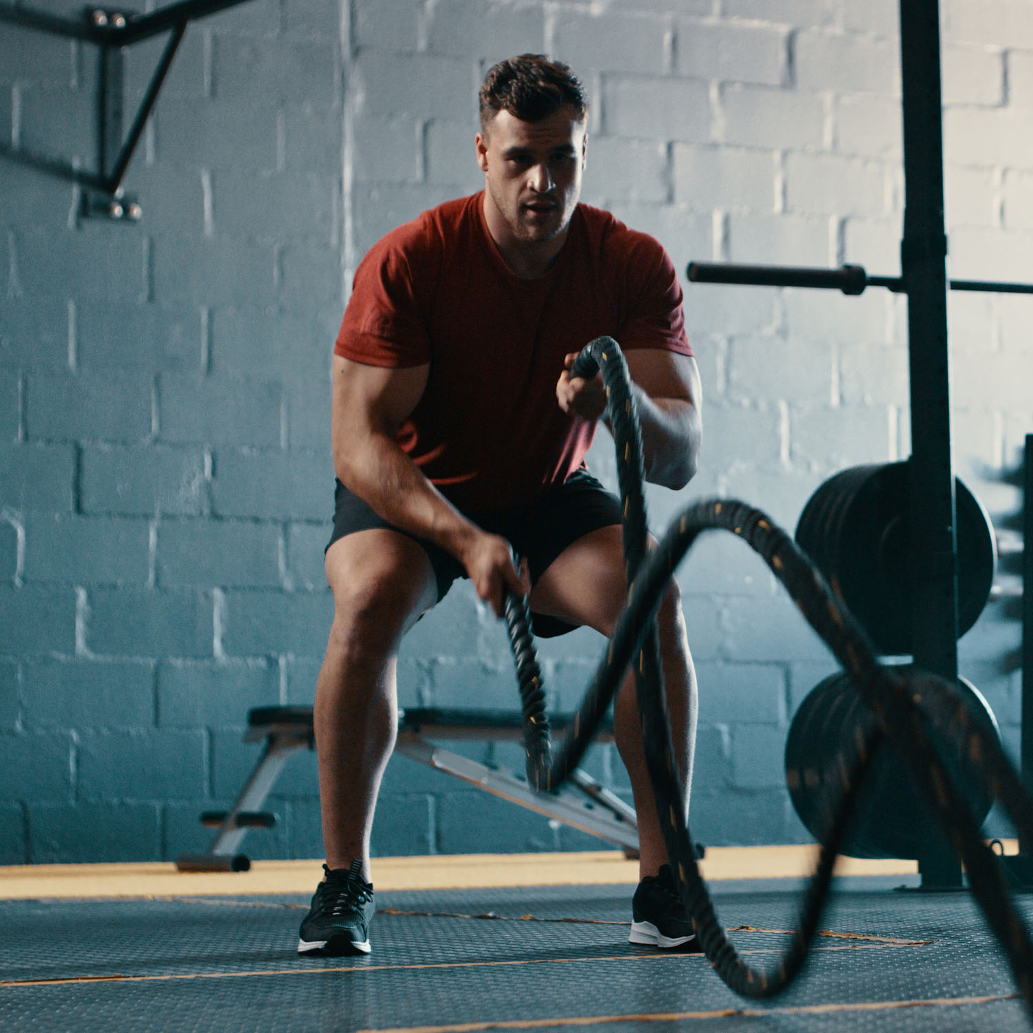 Ein junger Mann führt eine Übung mit Battle-Ropes in einem Fitnessstudio durch.
